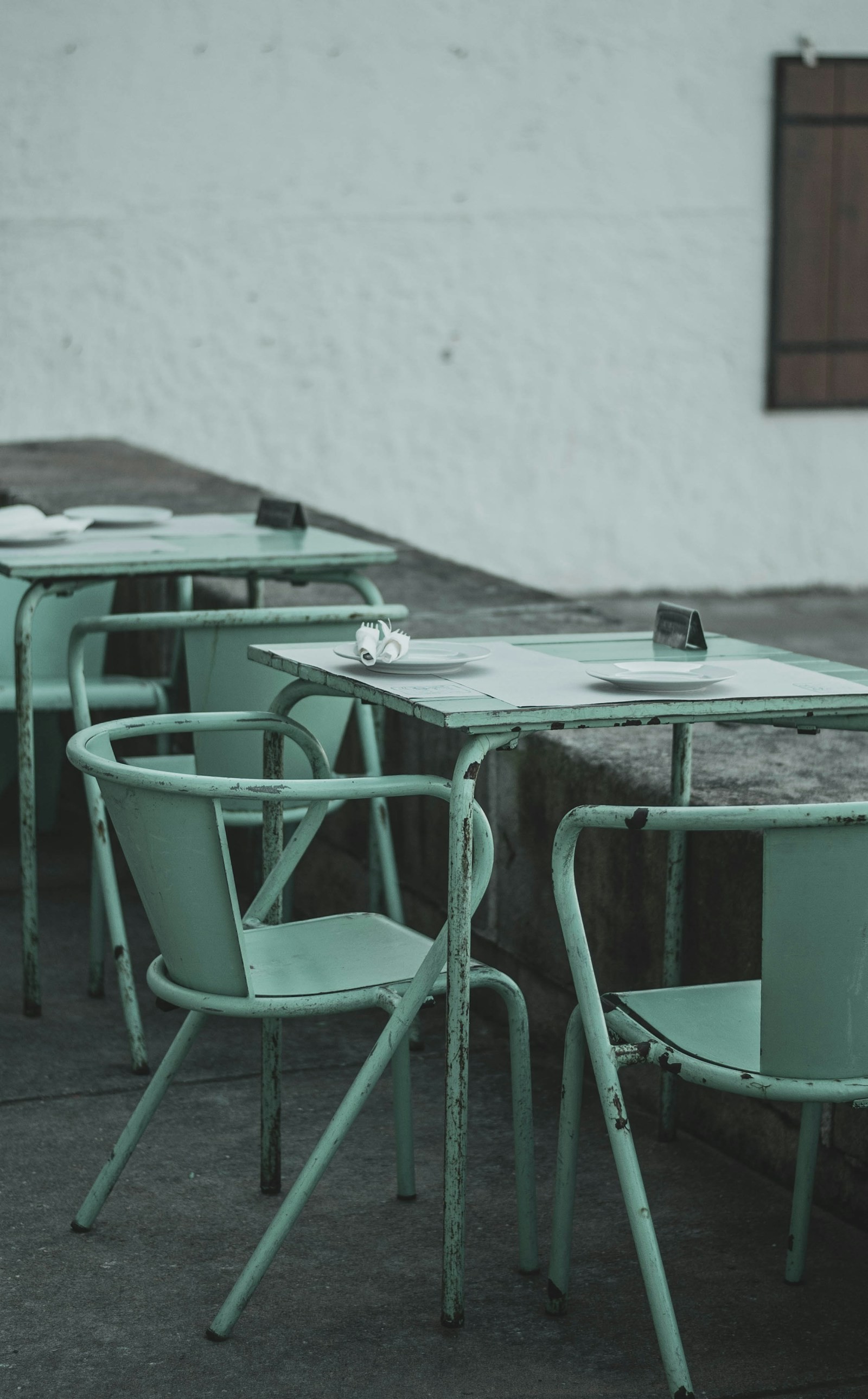 Sea-green café chairs and pale tables in a quiet Lisbon courtyard